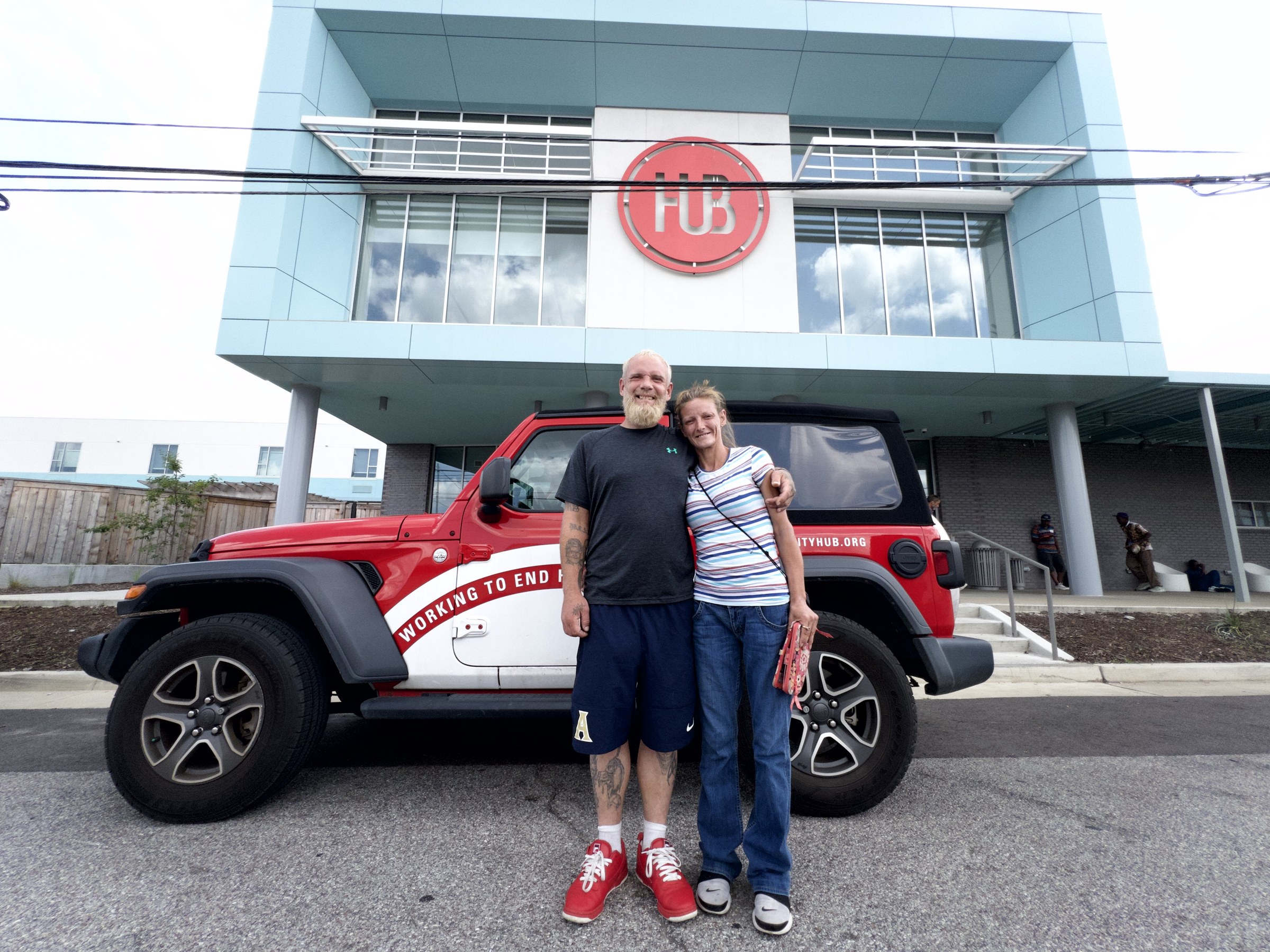 Two people standing beside the Hub outreach Jeep outside the Hospitality Hub